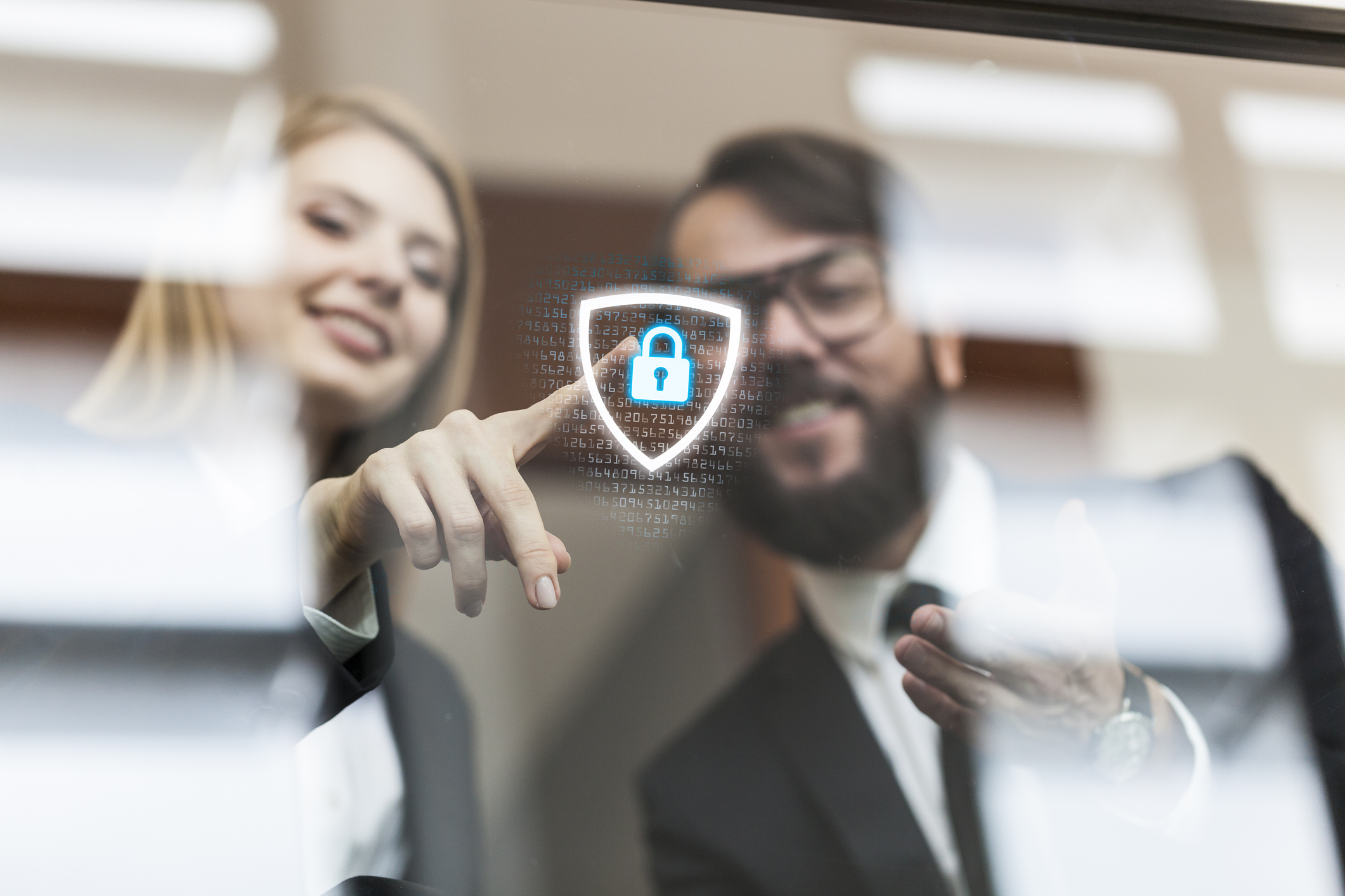 Zwei Geschäftsleute interagieren mit einem digitalen Sicherheitssymbol, das Datenschutz symbolisiert – symbolisch für den Einsatz eines Datenschutzbeauftragten im produzierenden Gewerbe.